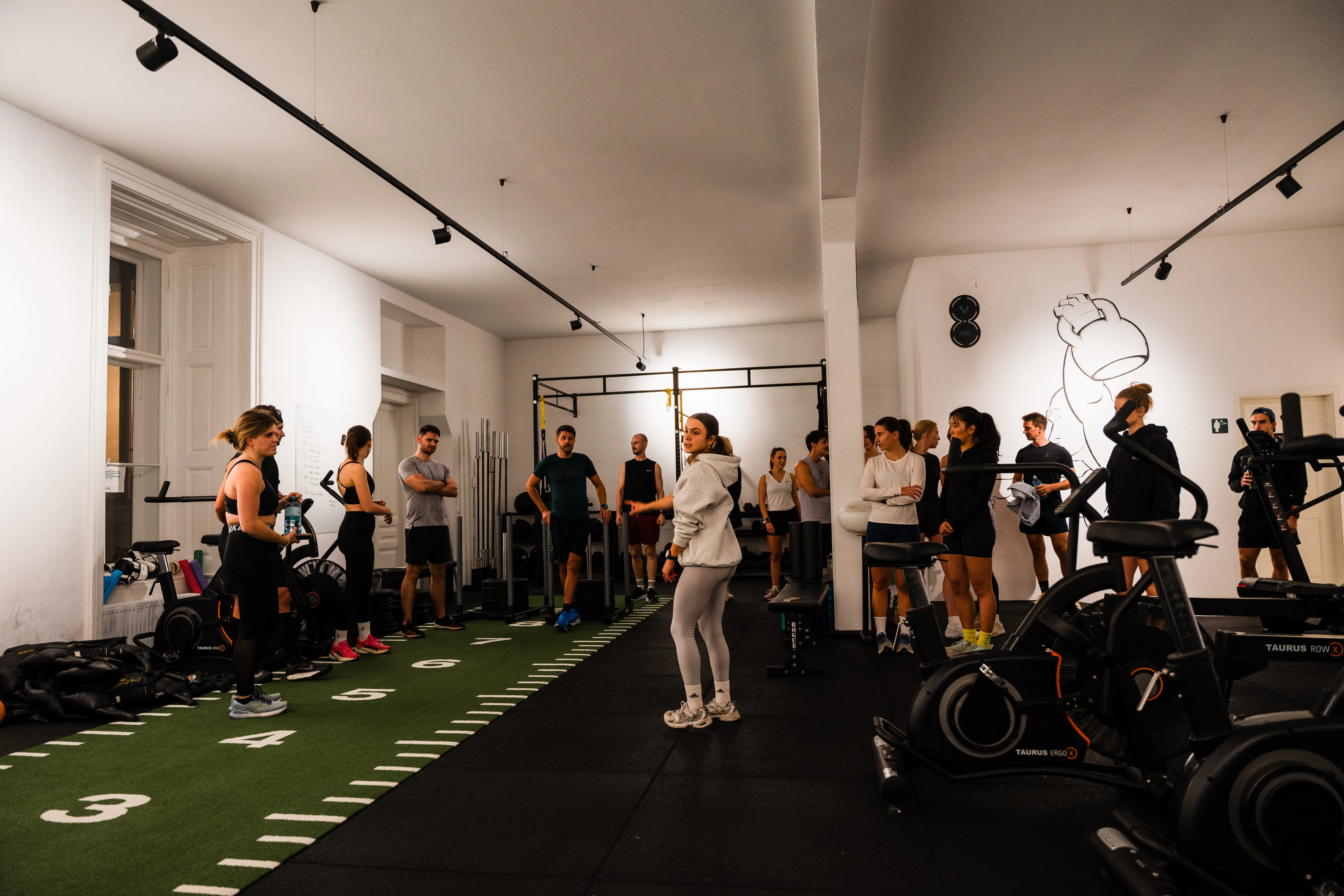 Helle Indoor-Halle mit Kunstrasen-Sprintbahn, Gruppe beim Briefing vor dem Training